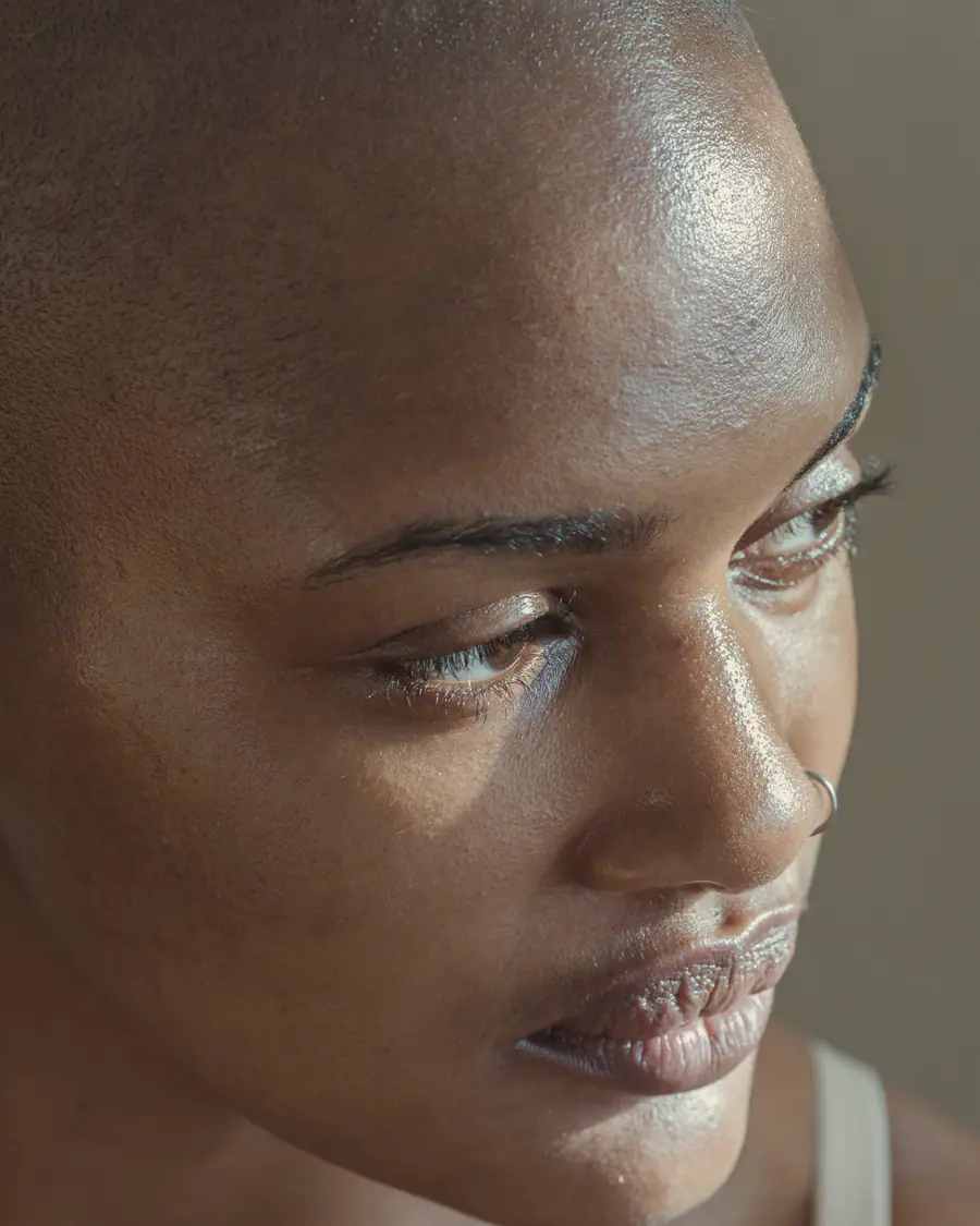 Rosto de mulher em luz lateral quente, olhando para baixo, com a pele em evidência.